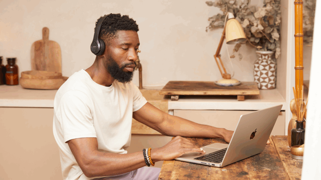 A man with headphones works focused on a laptop at a wooden table, learning how to sell supplements with print-on-demand.
