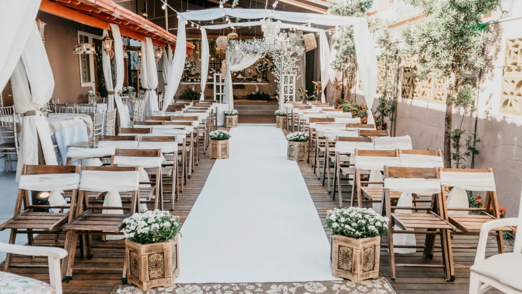 Event decor An outdoor wedding ceremony featuring wooden chairs arranged with white flowers adorning the aisle.