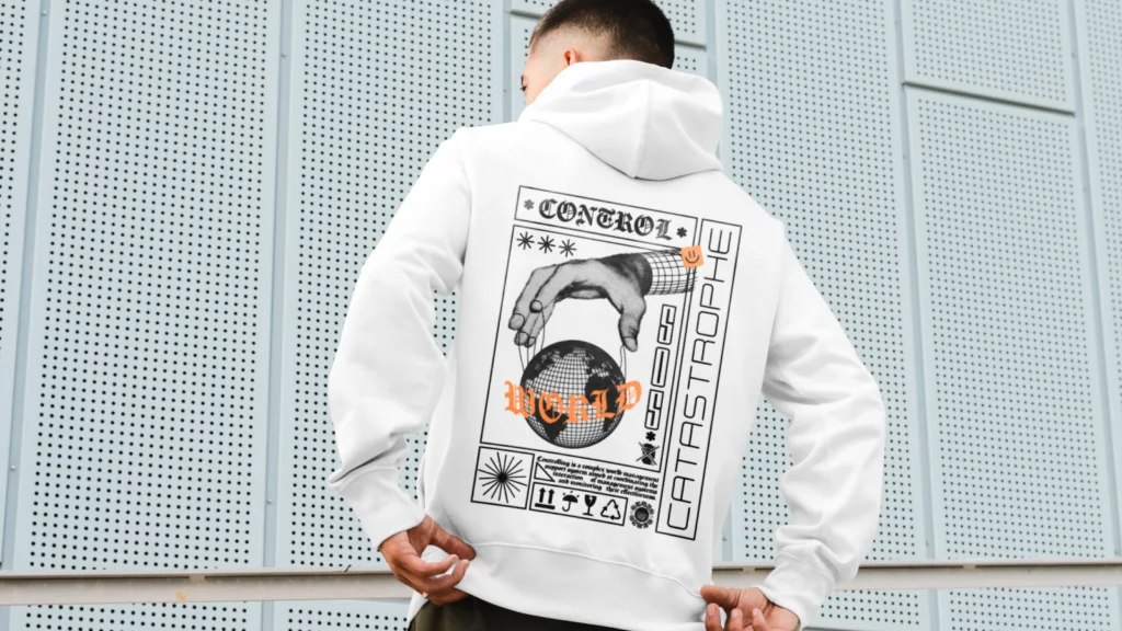 Futuristic and techwear inspired prints A man in a white hoodie with futuristic graphic designs on the back stands against a perforated metal wall.