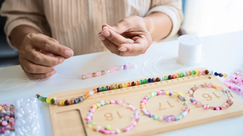 A woman is crafting a colorful bracelet using various beads on a table.