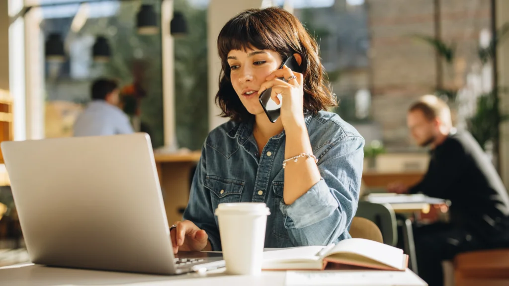 A woman sitting at a table, working on a laptop with a coffee cup beside her.