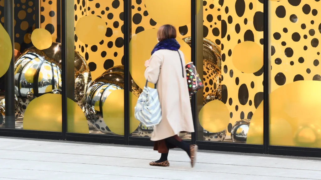 A woman walks past a window featuring a large gold and polka dot pattern, creating a vibrant visual contrast.