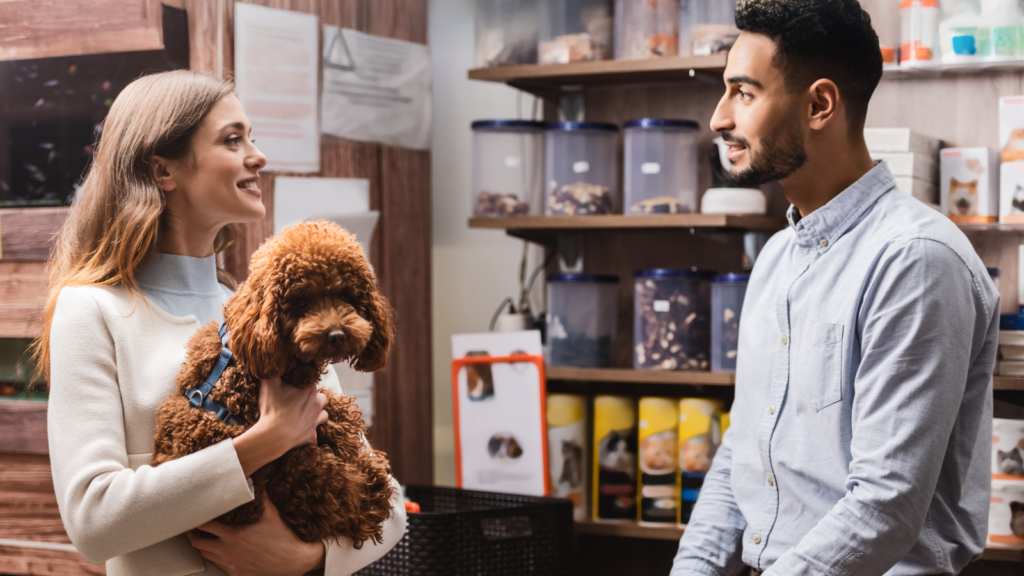 A man and woman stand outside a pet store, smiling and looking at the window displays filled with animals and pet supplies.