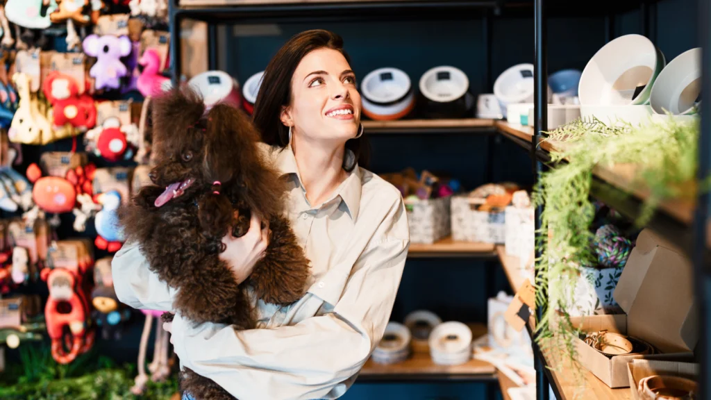 Pet products A woman holding a small dog while browsing in a pet store filled with various pet supplies.