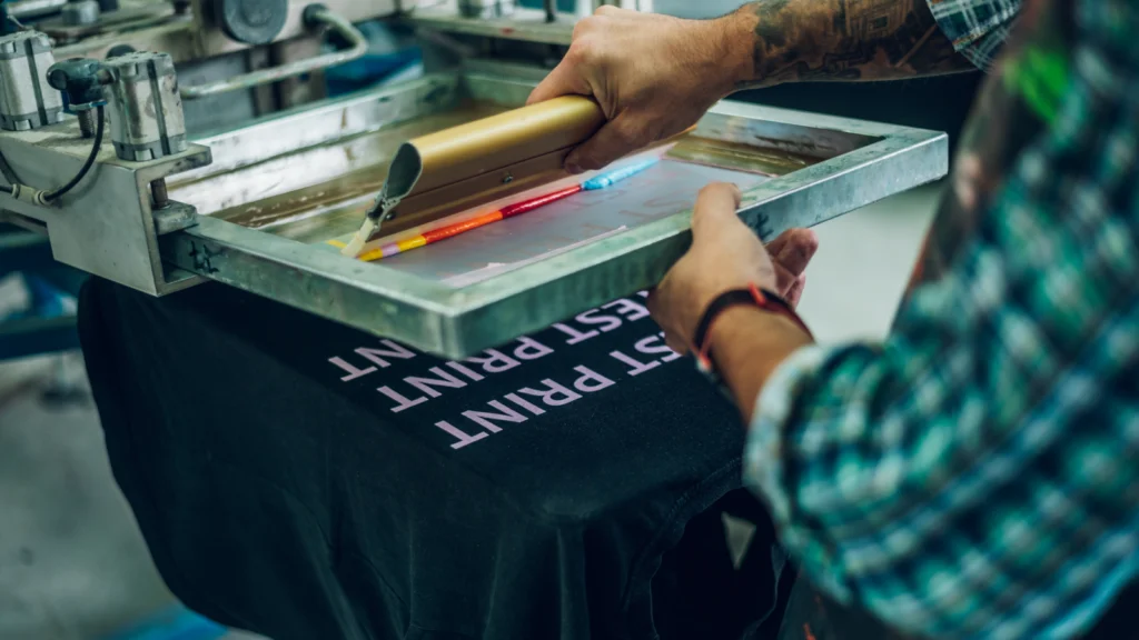 A man operates a printing machine to create a custom t-shirt design.