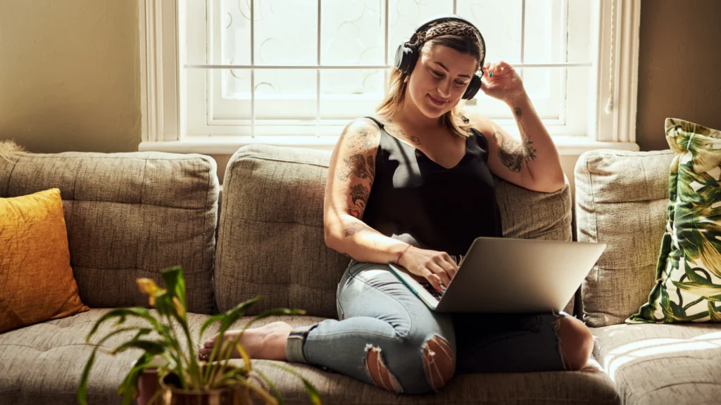 Publish to your store 2 A smiling woman in headphones is sitting with a laptop on her lap, using Printify’s Product Creator.