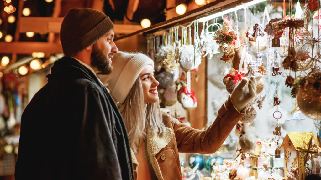 A couple admiring Christmas decorations at a festive market, surrounded by colorful lights and holiday cheer.