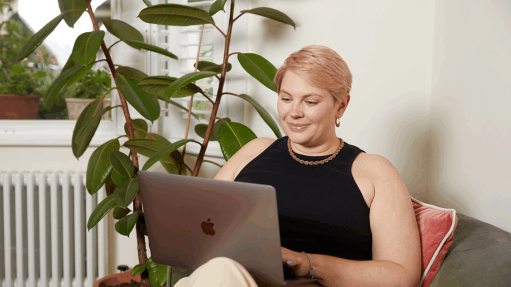 A woman with short hair sits comfortably on a couch, using a laptop to find out how to sell supplements.