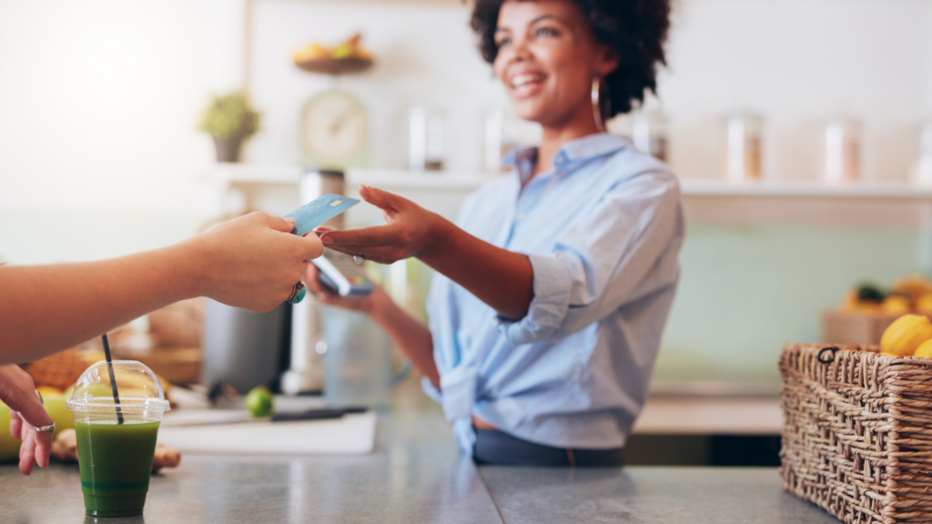 Step 4 Register your business licenses and permits A woman hands a credit card to another person in a transaction setting.