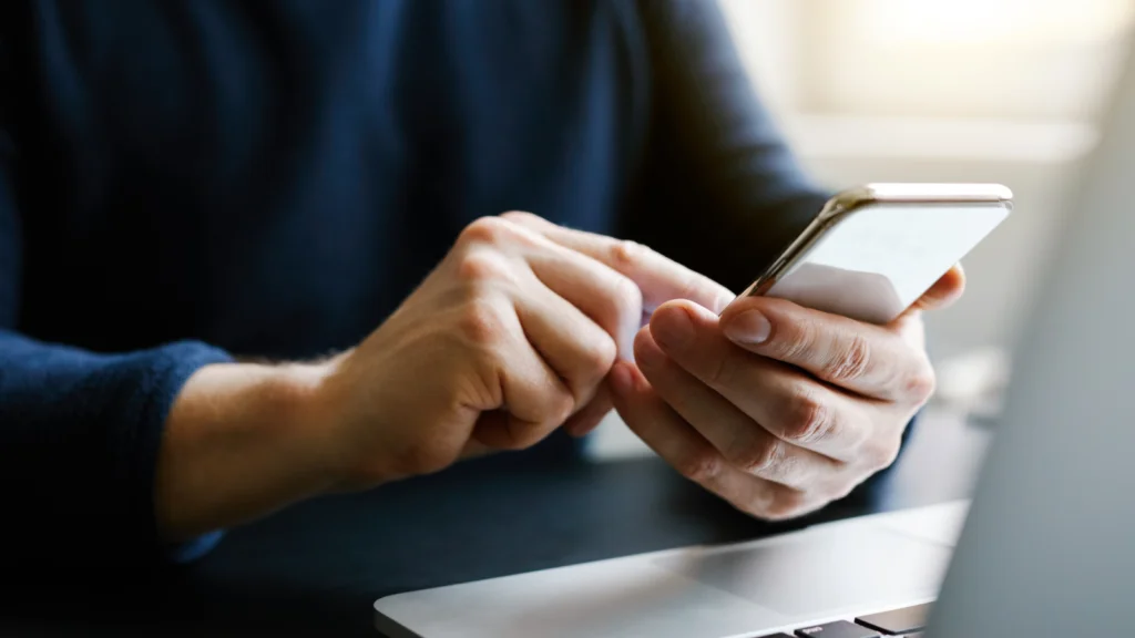 A person sitting at a desk, holding a cell phone and looking at the screen with a focused expression.