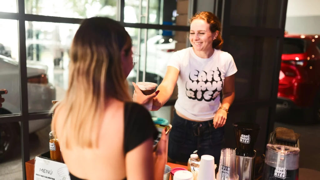 A woman serves coffee to another woman at a cozy café table, both smiling and enjoying their time together.