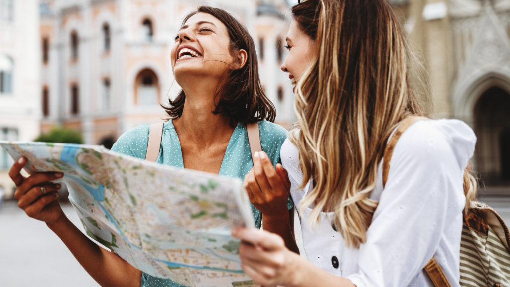 Two women smiling while examining a map together, enjoying their time and planning their route.