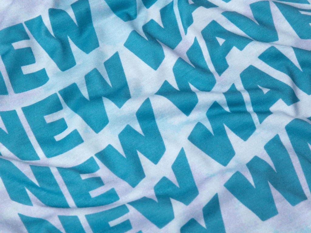 A close-up of a fabric with bold, teal "NEW WAVE" text on a light background.