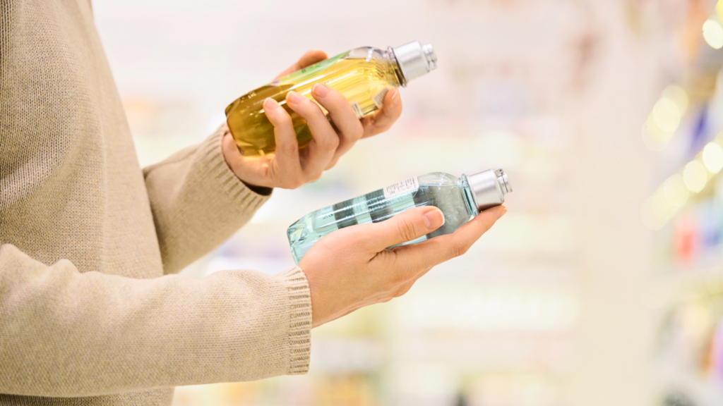 A person in a beige sweater holds two colorful bottles, one gold and one blue, in a store aisle.