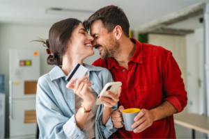 A man and woman smile while holding their credit cards, showcasing excitement about their purchase.