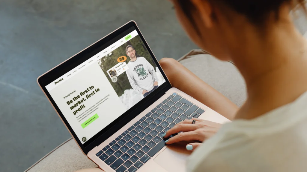 A man is using a laptop with Printify’s homepage on the screen.