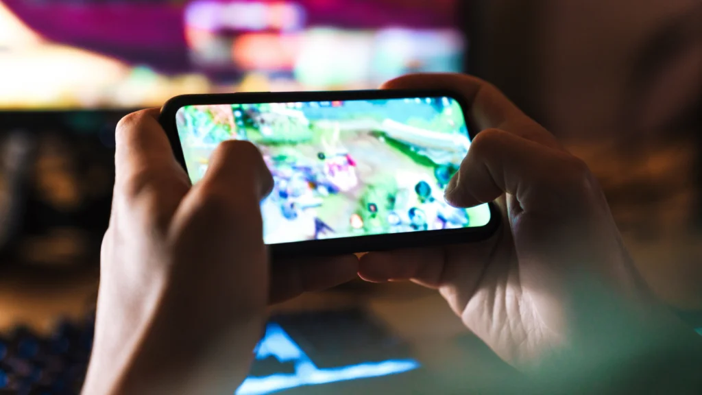 Hands holding a smartphone horizontally, displaying a brightly colored game. The background is blurred.