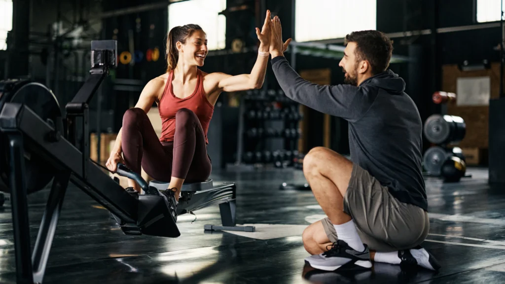 A man and woman high five each other in a gym, celebrating a successful workout together.