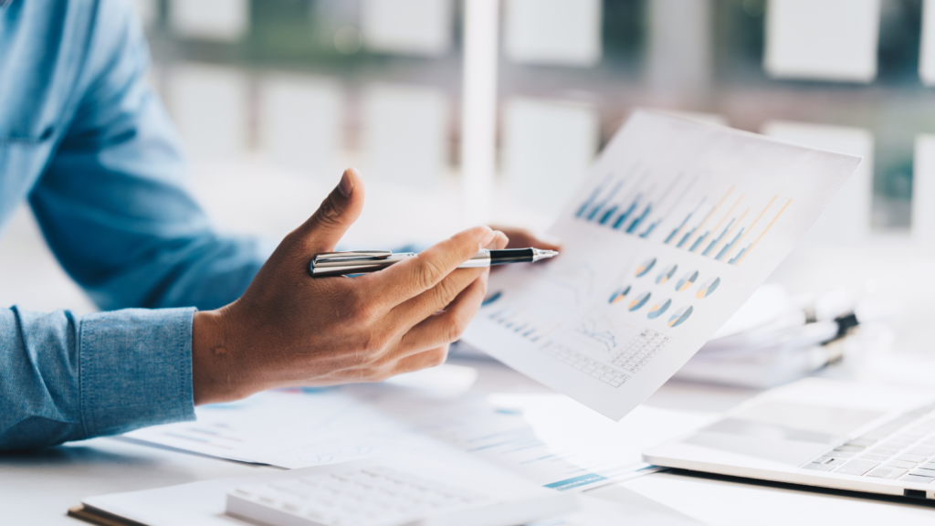 Businessman's hands analyzing graphs and documents on a desk, indicating financial data and strategic planning.