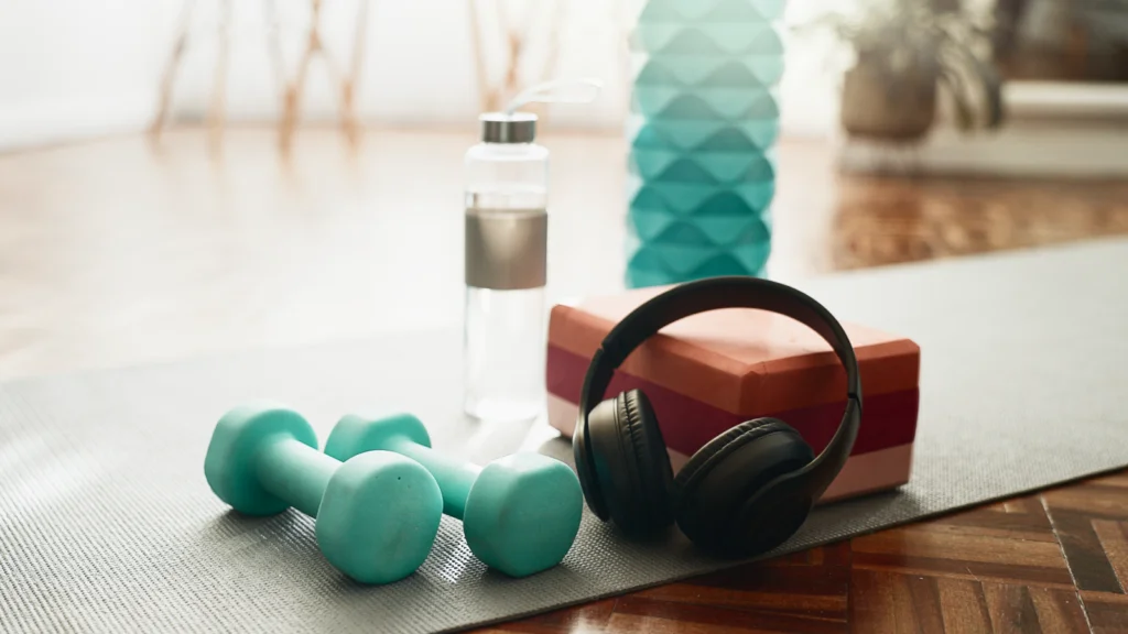 A pair of headphones, a water bottle, and a dumbbell are arranged on a yoga mat, suggesting a fitness setting.