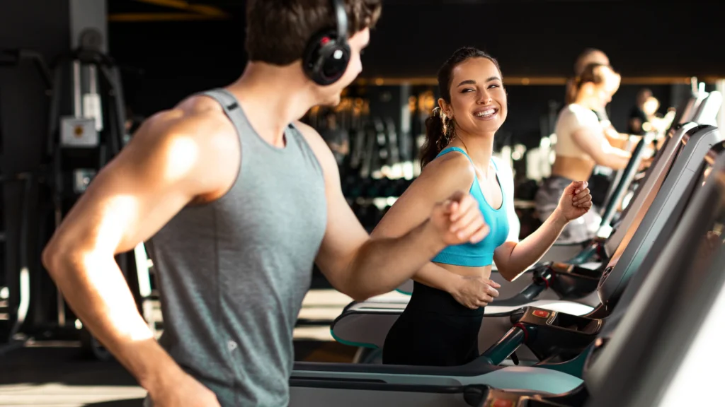 A man and woman jogging side by side on treadmills in a gym setting.