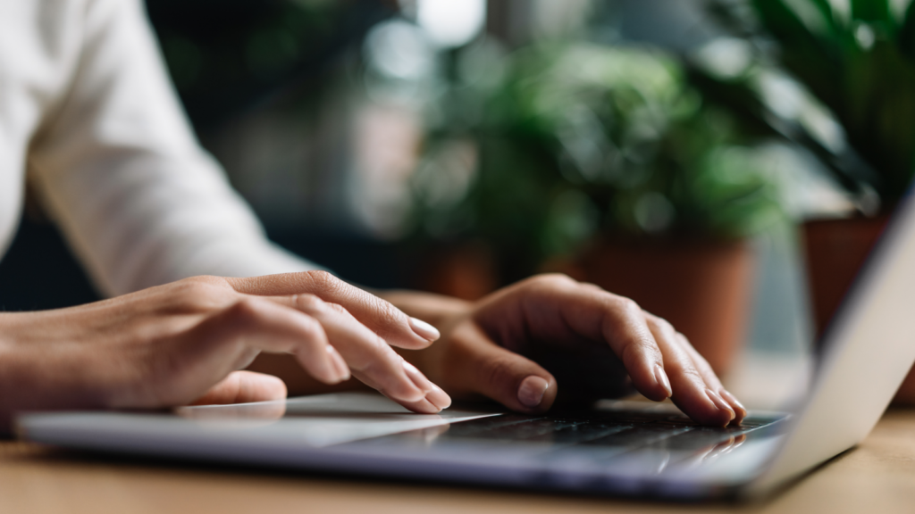 A person focused on typing on a laptop computer, with hands positioned over the keyboard.