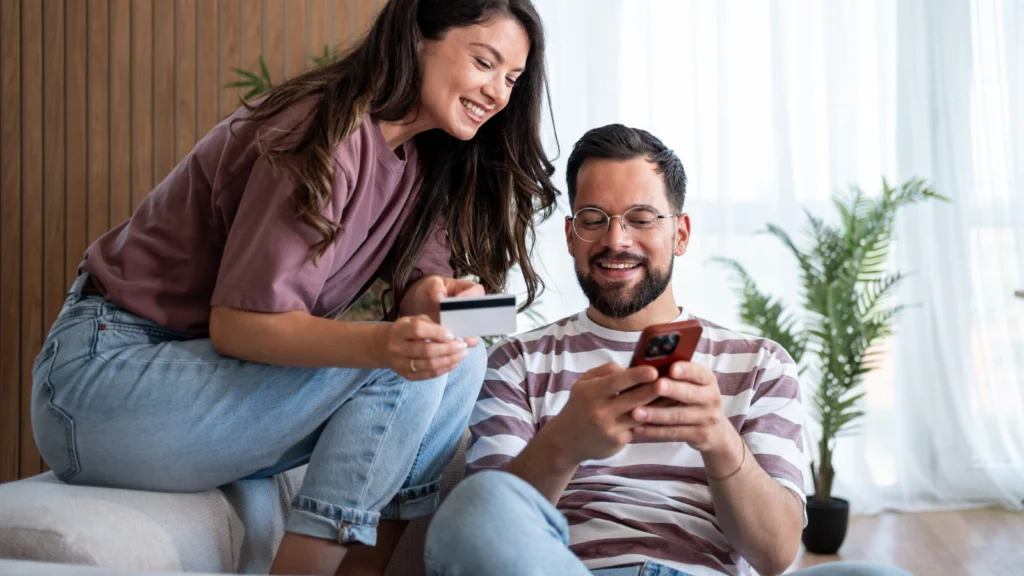 A young couple engaged in making a purchase on their smartphones, focused on their screens in a casual setting.