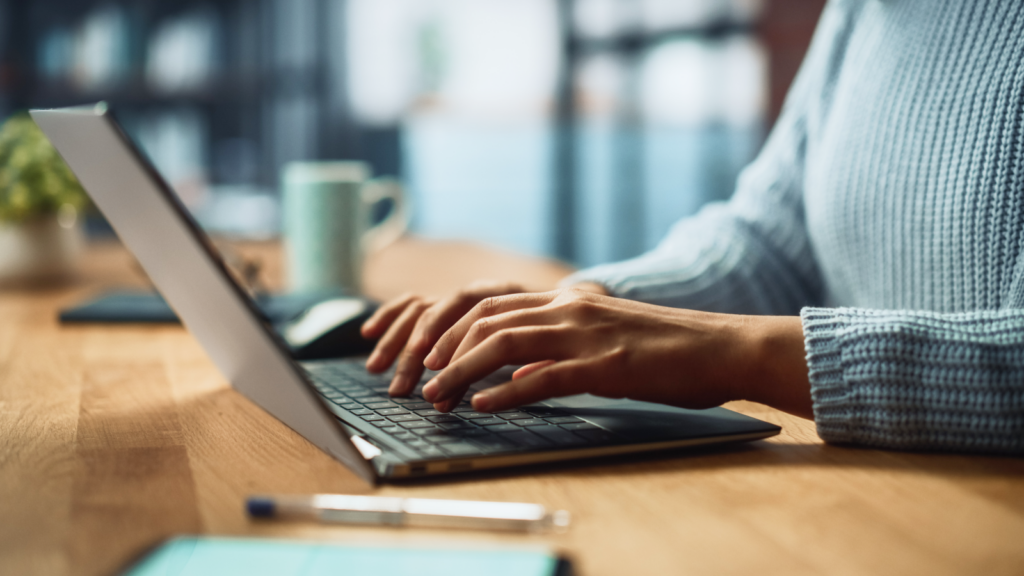 A person focused on typing on a laptop computer, with hands positioned over the keyboard.