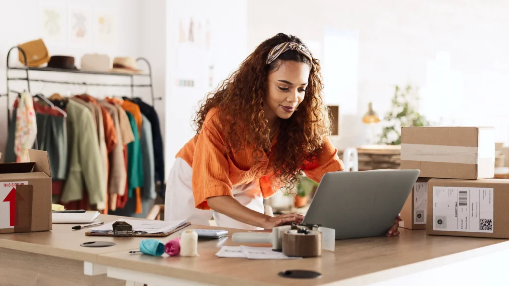 A woman focused on her laptop in a room filled with unpacked boxes, indicating a recent move or organization.