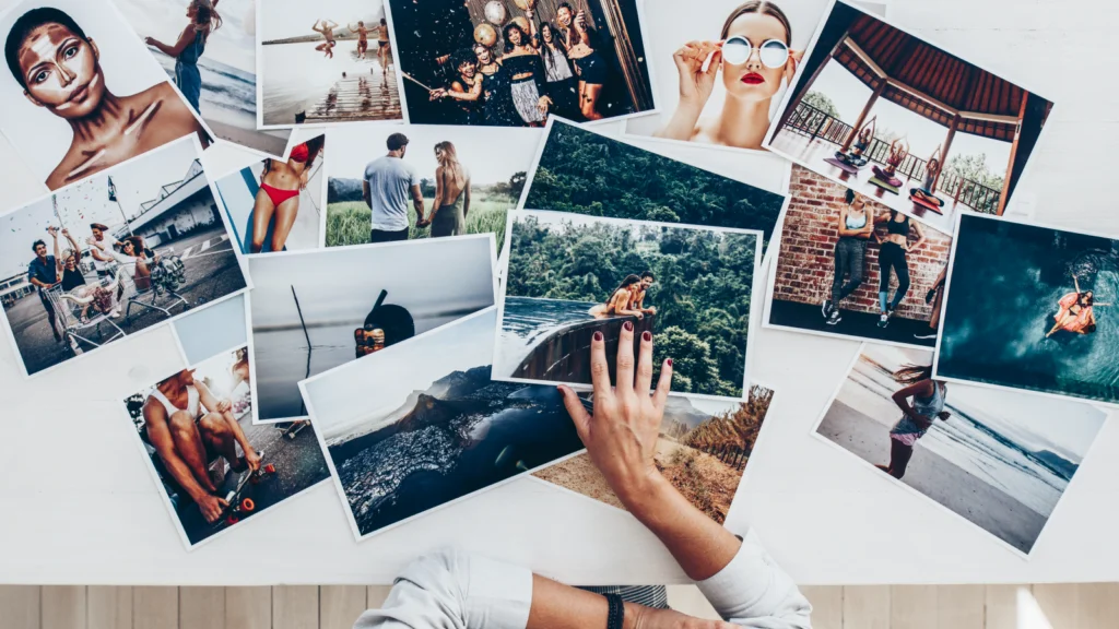 Hands arranging various vibrant photographs on a table. Images include people at the beach, a woman in sunglasses, and scenic views.