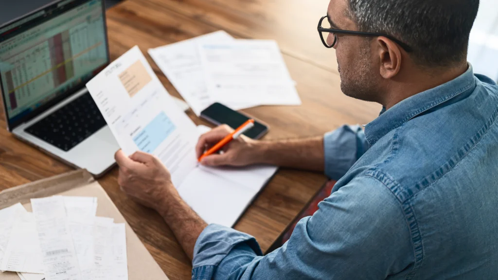 Man focused on paperwork while seated at a desk, surrounded by office supplies and a computer.