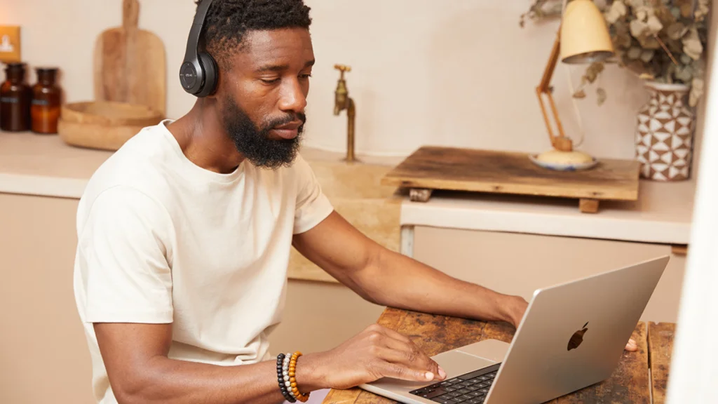 A bearded man wearing headphones is focused on working on his laptop.