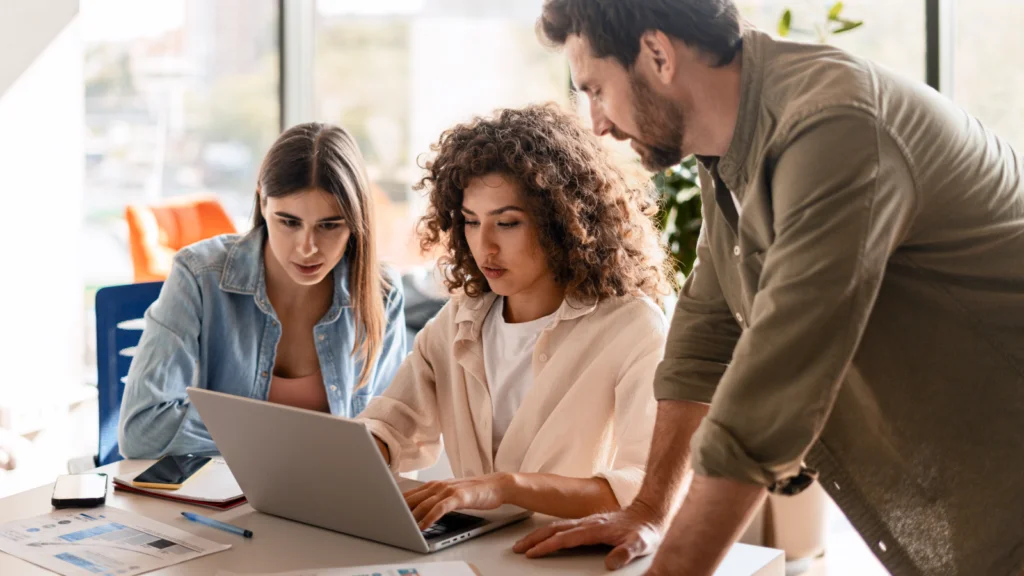 Three colleagues collaborating on a laptop in a modern office setting.