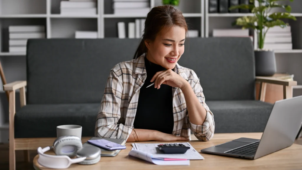 A woman sitting at a table, working on a laptop with a cup of coffee beside her.