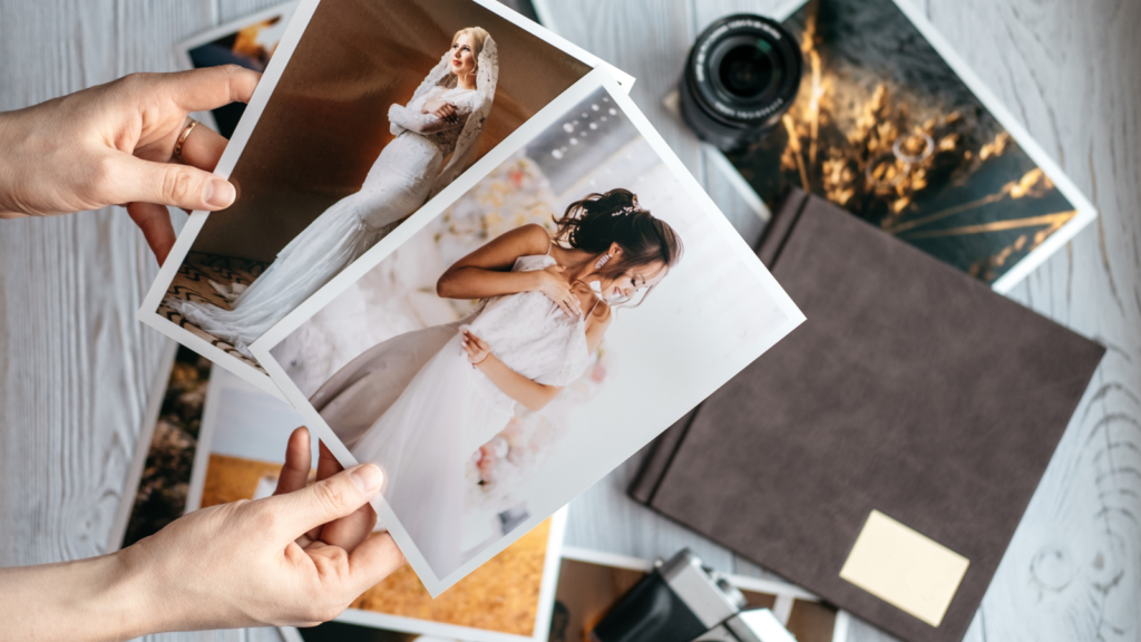 Two hands hold wedding photos of a bride and a girl in white dresses. Nearby are more photos, a camera, and a photo album.