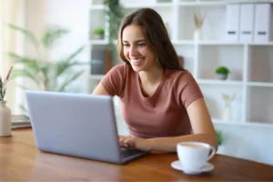 A woman smiles while working on a laptop, conveying a sense of joy and engagement with her task.