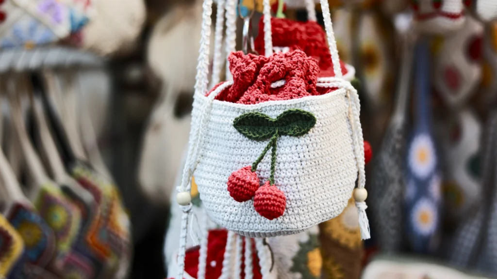 04 Crochet bags A white crocheted bag with a red cherry design hangs among colorful fabric items.