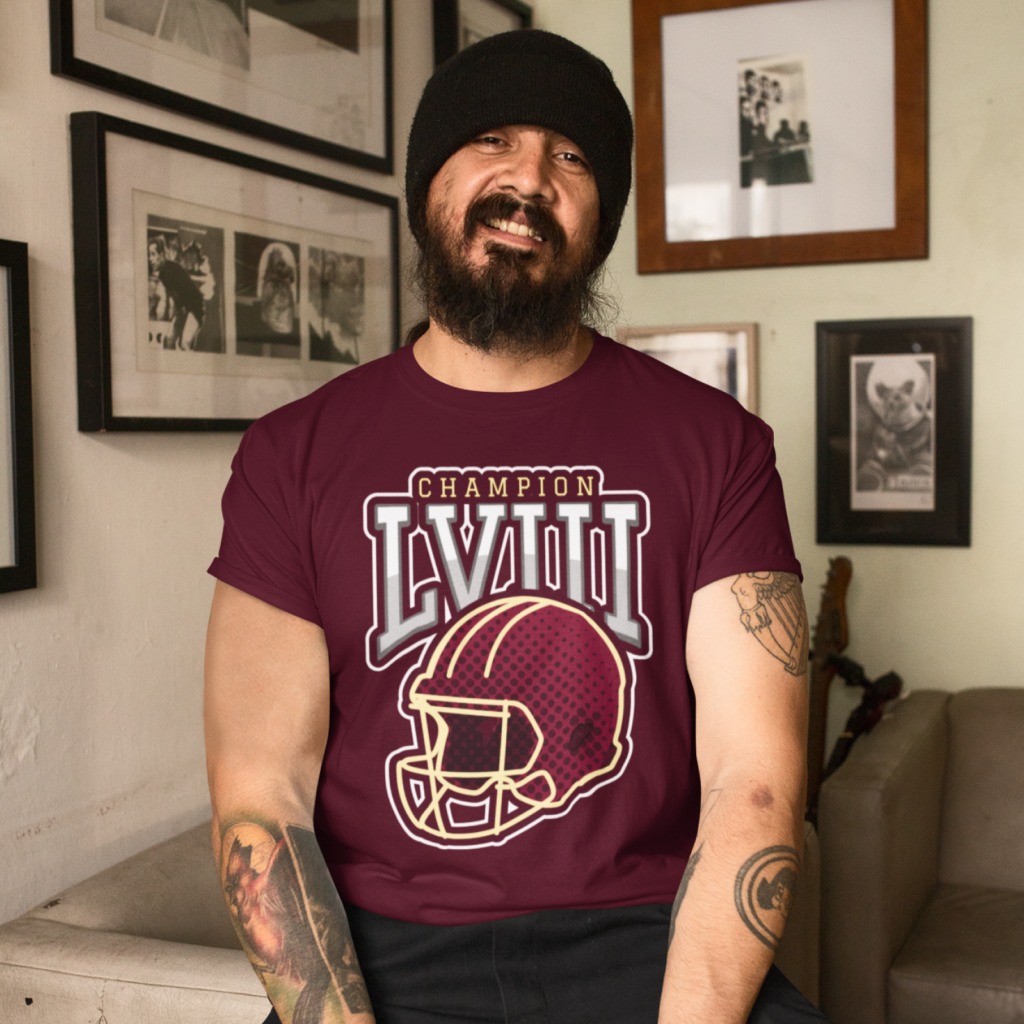 04 Roman numeral championship tee A man with a beard and tattoos, wearing a maroon "Champion LVIII" football helmet shirt, smiles indoors.