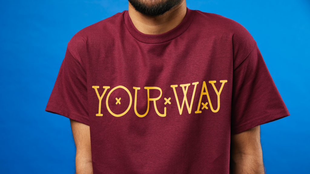 A man wearing a maroon t-shirt with "YOUR WAY" in yellow letters. The background is solid blue.