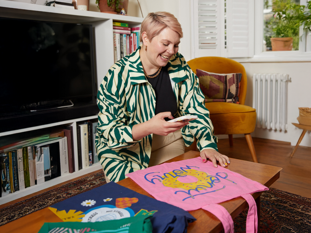 A woman seated at a table with a bag of clothes beside her, appearing engaged in thought or conversation.
