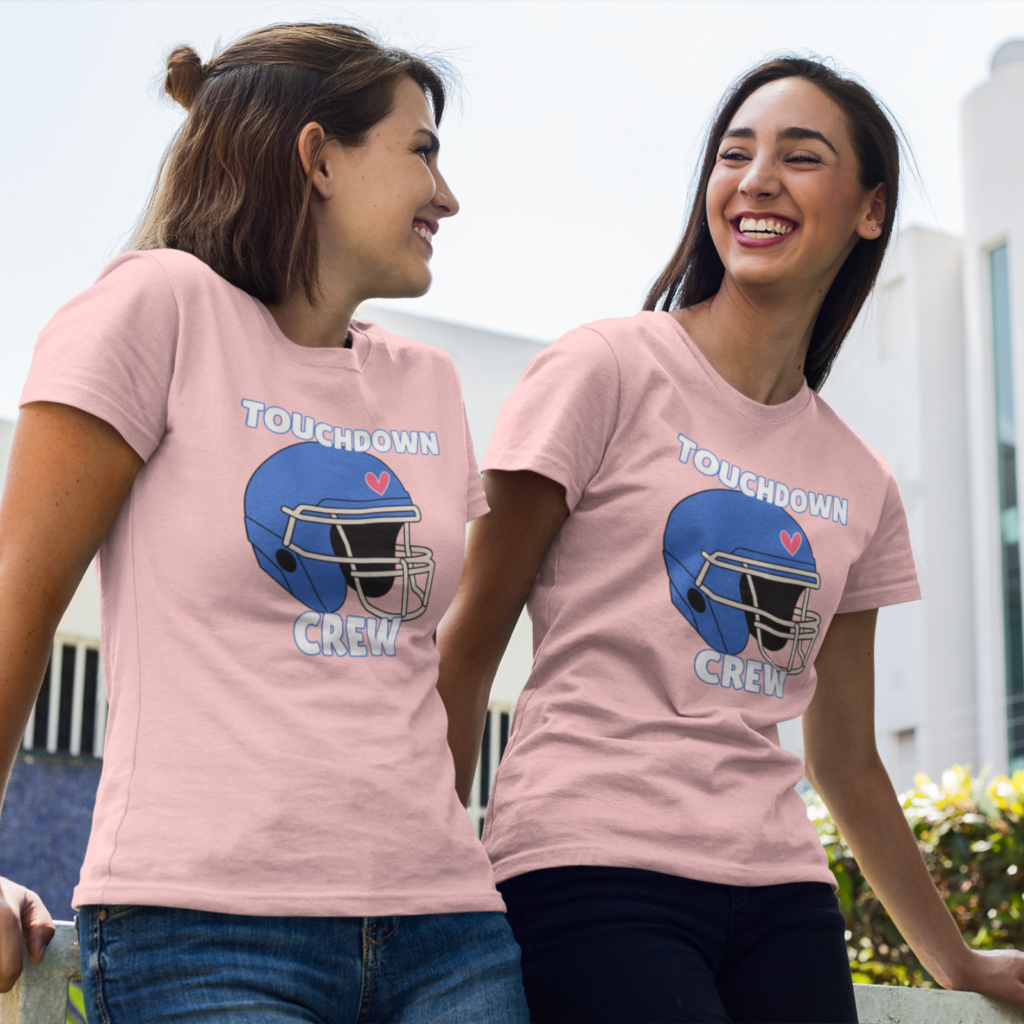11 Super Bowl matching tees Two women smiling at each other, wearing matching pink t-shirts with a blue football helmet design and the words “Touchdown Crew”.