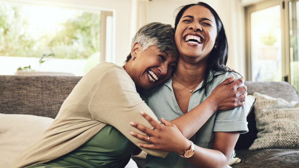 Two women embrace warmly while sitting together on a cozy couch.