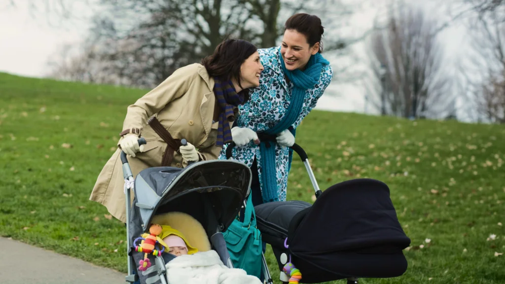 Two friends walking outside with babies in their strollers.
