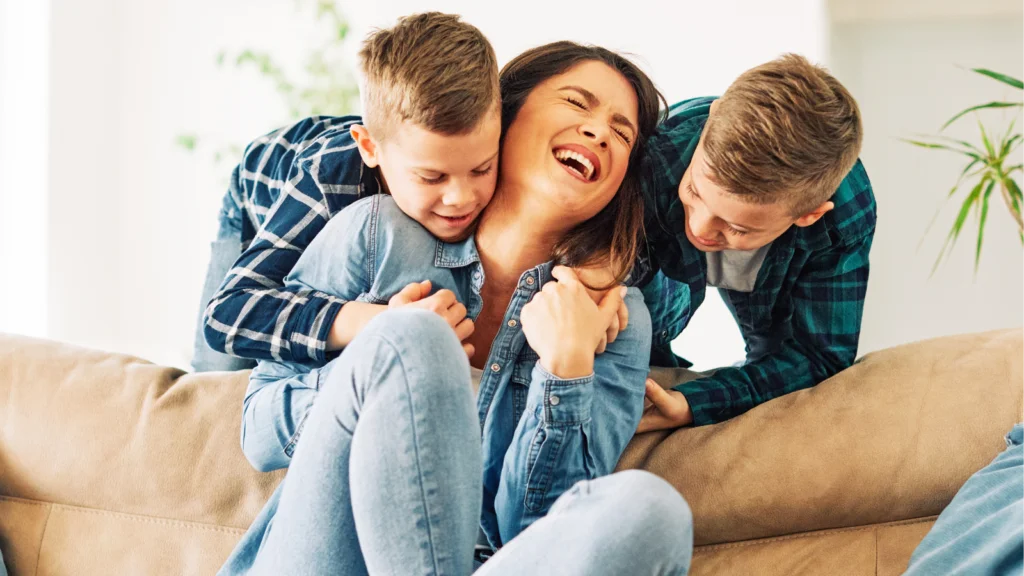 A woman and two boys are sitting together on a couch, smiling and enjoying each other's company.