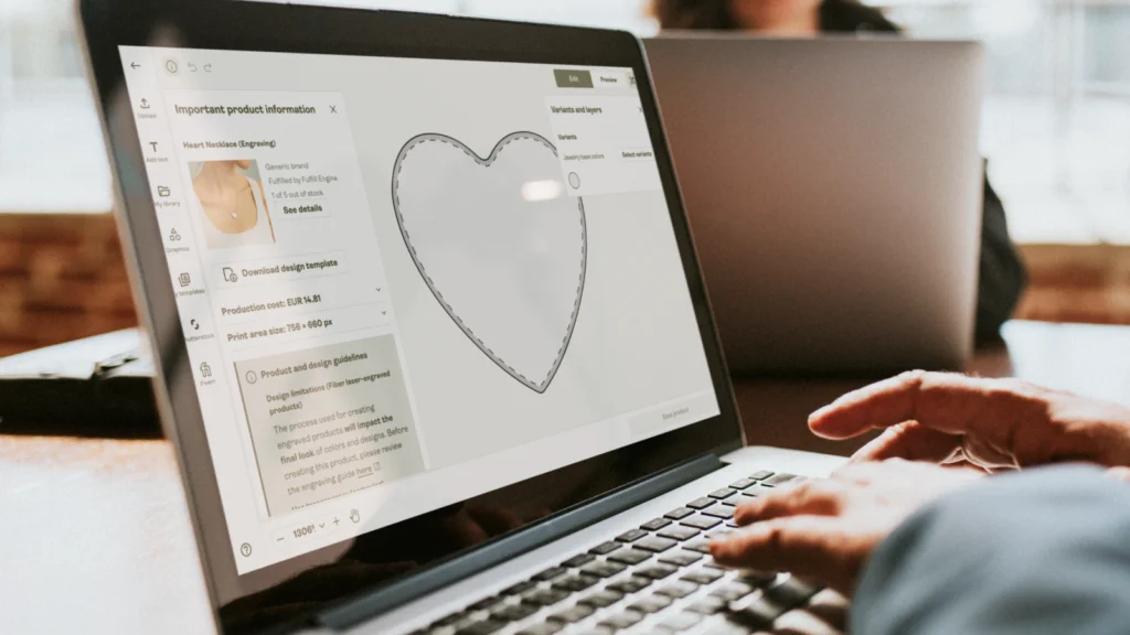 A person uses a laptop displaying Printify’s Product Creator with a heart-shaped piece of jewelry being designed.