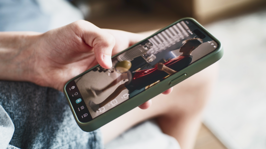 A person holds a smartphone, viewing a video of a boy in a red shirt sitting indoors.