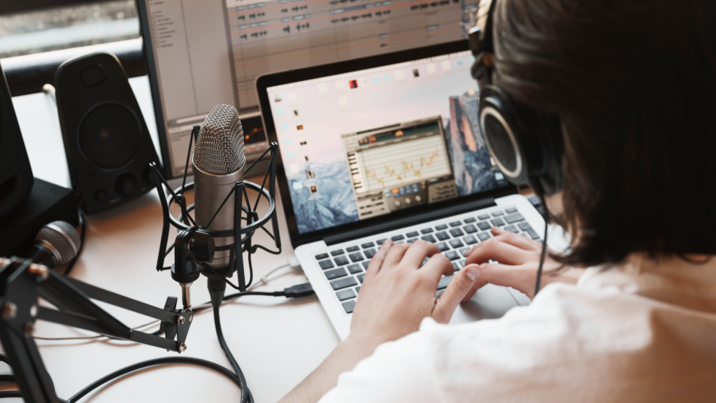 A person wearing headphones is editing a podcast, surrounded by audio equipment including a microphone and speakers.
