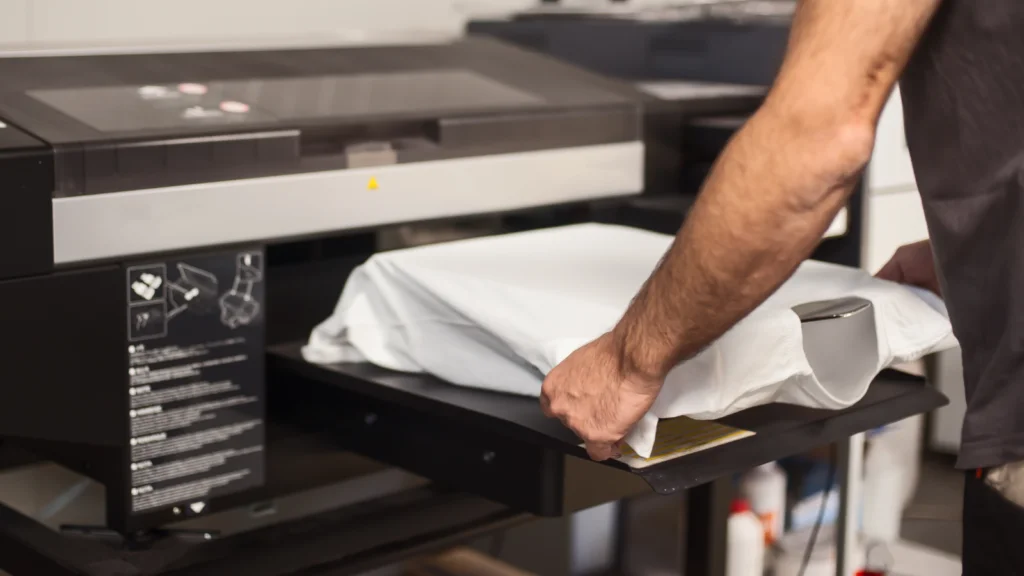 03 How is a Print Provider selected for an order A person prepares a white garment on a digital printing machine, focusing on precise placement.