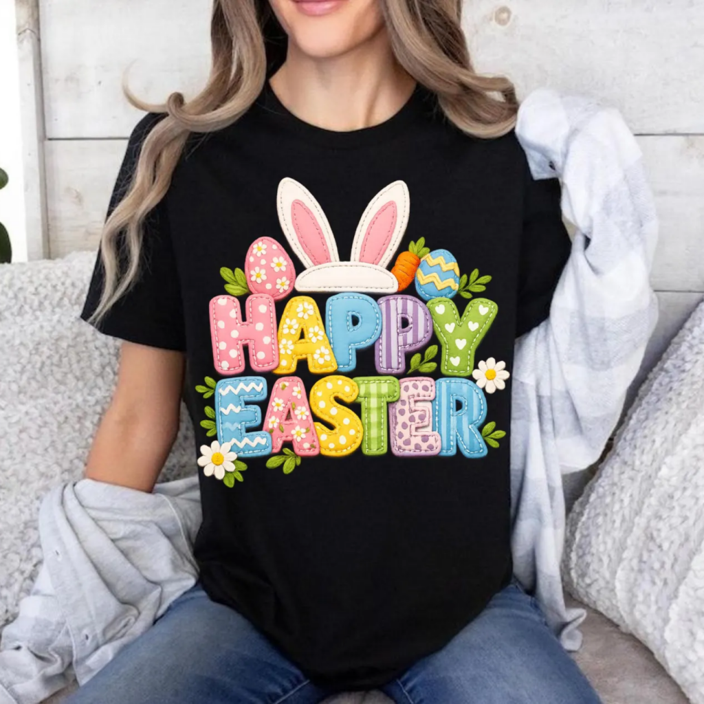 A woman wearing a black t-shirt with colorful "Happy Easter" text, adorned with bunny ears, Easter eggs, and flowers.