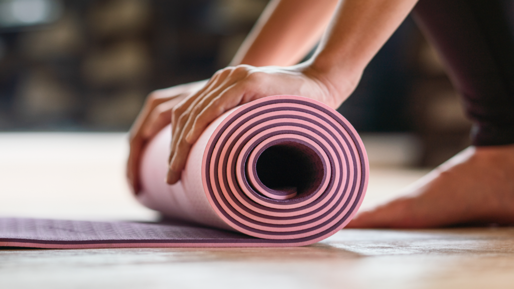 Close-up of hands rolling a striped pink yoga mat on a hardwood floor.